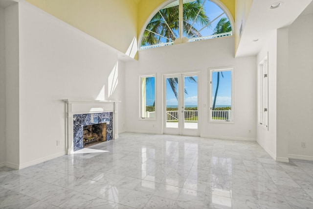 unfurnished living room with a high ceiling, marble finish floor, baseboards, and a high end fireplace