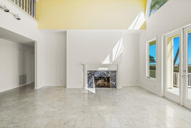 unfurnished living room featuring a healthy amount of sunlight, a tile fireplace, marble finish floor, and a towering ceiling