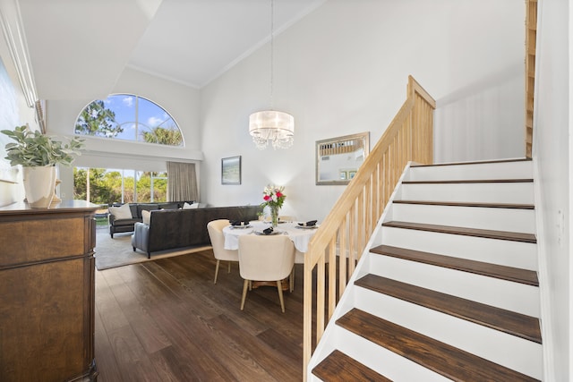 staircase featuring high vaulted ceiling, an inviting chandelier, dark hardwood / wood-style flooring, and ornamental molding