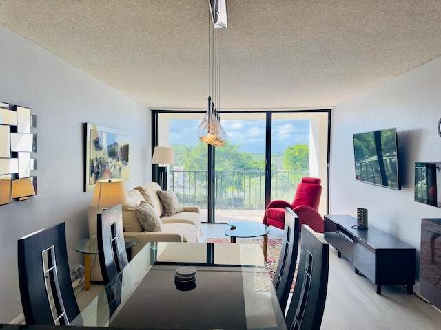 dining room with plenty of natural light, floor to ceiling windows, light wood-type flooring, and a textured ceiling