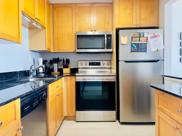 kitchen with light wood-type flooring, appliances with stainless steel finishes, sink, and dark stone countertops