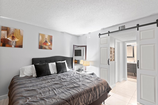 bedroom featuring ensuite bathroom, light tile patterned flooring, and a textured ceiling