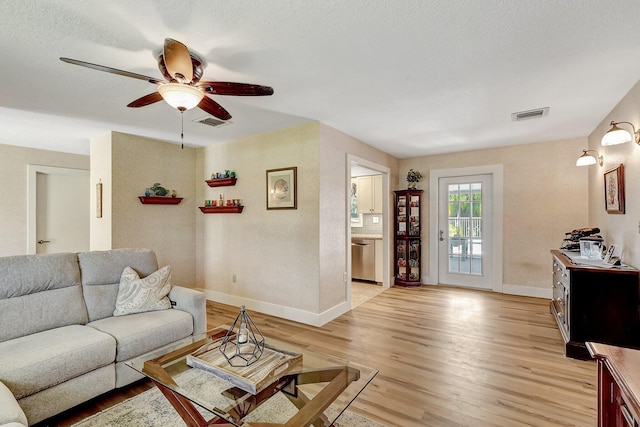 living room with ceiling fan, light hardwood / wood-style flooring, and a textured ceiling