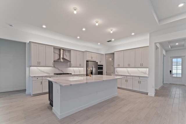 kitchen featuring wall chimney exhaust hood, gas stovetop, stainless steel fridge, light stone countertops, and a kitchen island with sink