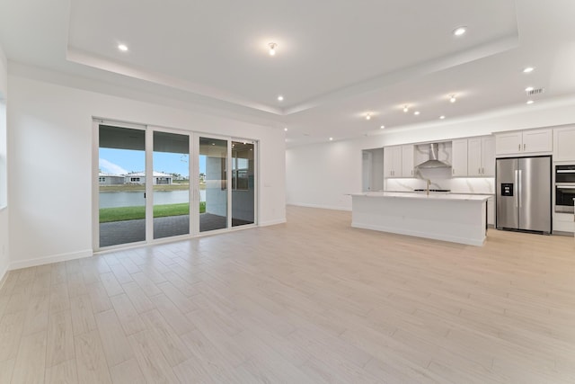 unfurnished living room with a water view, a raised ceiling, and sink