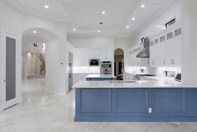 kitchen featuring stainless steel appliances, wall chimney range hood, kitchen peninsula, white cabinets, and ornamental molding