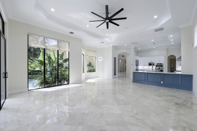 unfurnished living room featuring a raised ceiling, ceiling fan, and ornamental molding