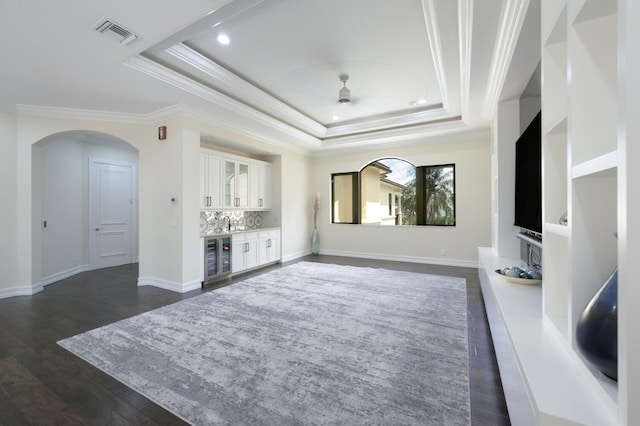 unfurnished living room featuring a raised ceiling, ceiling fan, dark wood-type flooring, and ornamental molding