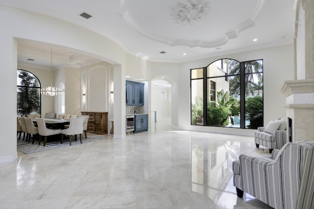 living room with beverage cooler, an inviting chandelier, a raised ceiling, crown molding, and a fireplace