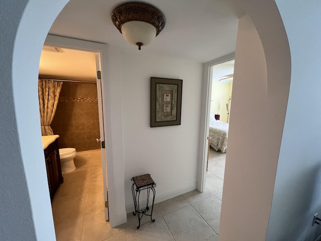 hallway featuring baseboards, arched walkways, and light tile patterned flooring