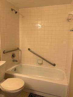 bathroom featuring tile patterned flooring, tiled shower / bath combo, and toilet