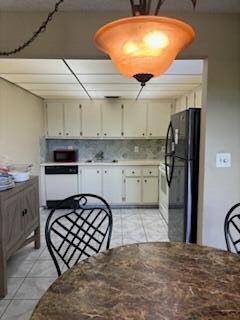 kitchen featuring black fridge, backsplash, cream cabinets, white dishwasher, and light tile patterned floors