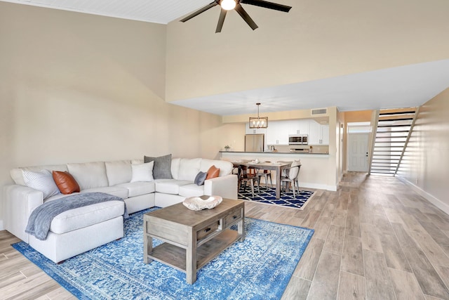 living room featuring ceiling fan with notable chandelier and light wood-type flooring