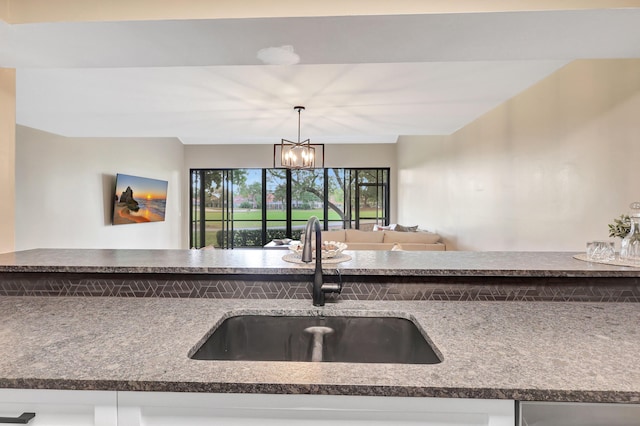 kitchen with sink, white cabinets, pendant lighting, and an inviting chandelier