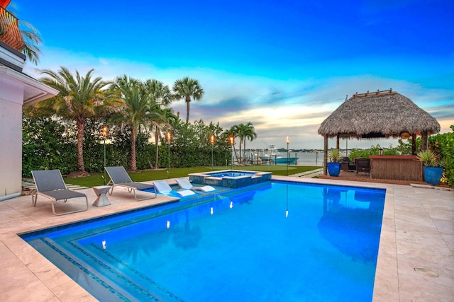 pool at dusk with a gazebo, a water view, an in ground hot tub, and a patio area