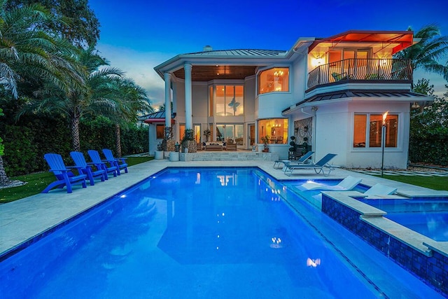 back house at dusk with a swimming pool with hot tub, a patio, and a balcony