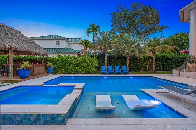 pool at dusk with a gazebo, an in ground hot tub, and a patio