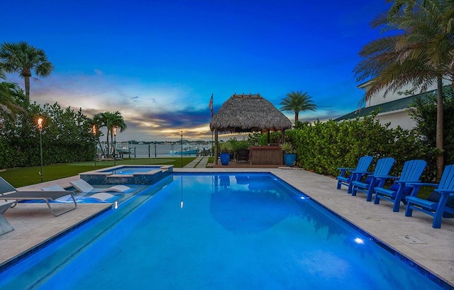 pool at dusk featuring a gazebo, an in ground hot tub, and a patio