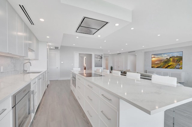 kitchen featuring tasteful backsplash, sink, white cabinets, a kitchen bar, and a large island