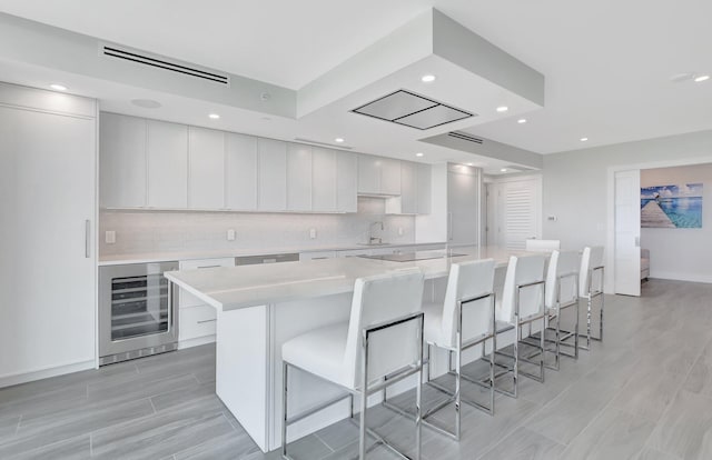 kitchen featuring white cabinetry, a spacious island, beverage cooler, and tasteful backsplash