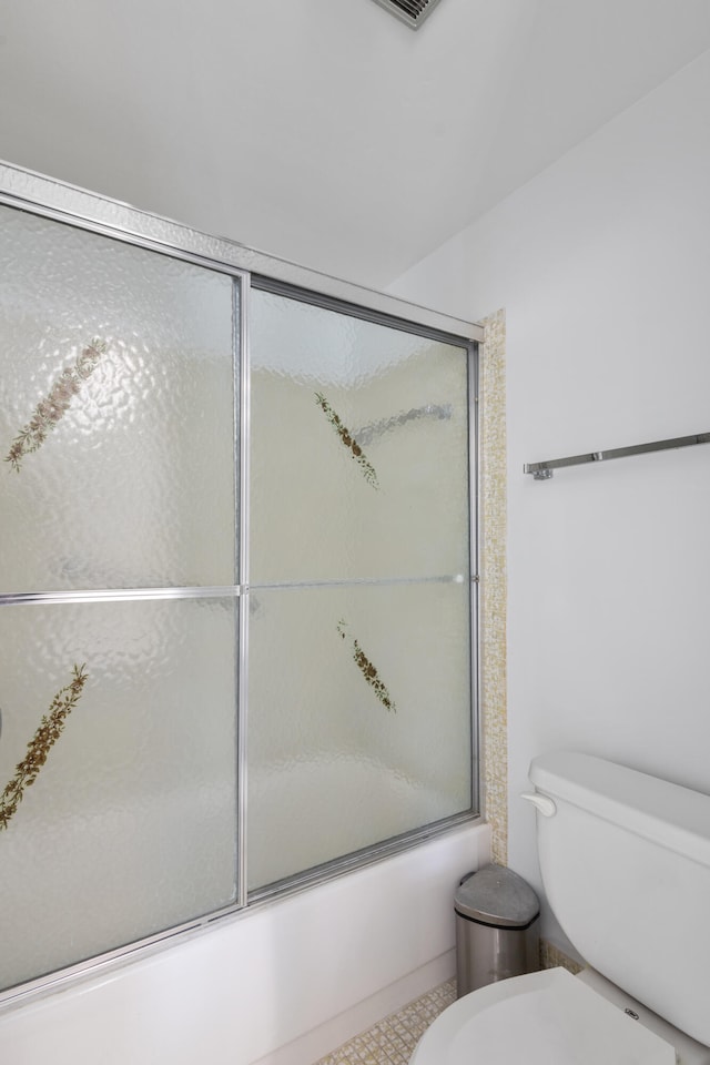 bathroom with tile floors, toilet, and bath / shower combo with glass door