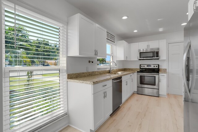 kitchen with appliances with stainless steel finishes, white cabinetry, plenty of natural light, and light hardwood / wood-style flooring