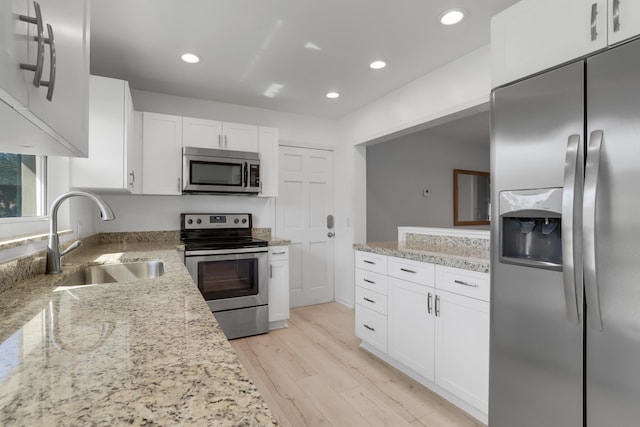 kitchen with stainless steel appliances, light wood-type flooring, light stone counters, sink, and white cabinets