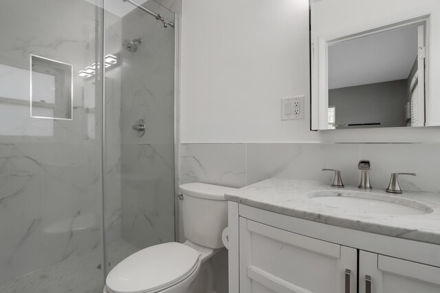 bathroom with tile walls, a shower with shower door, toilet, and vanity with extensive cabinet space