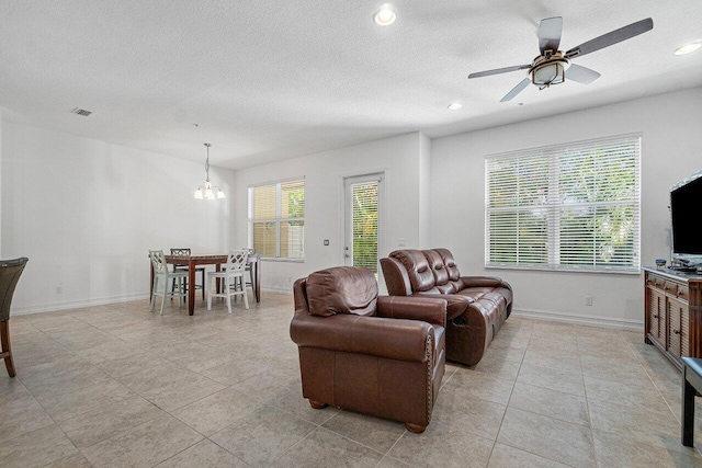 tiled living room with a textured ceiling and ceiling fan with notable chandelier