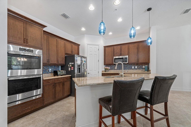 kitchen with pendant lighting, a breakfast bar, sink, stainless steel appliances, and light stone counters