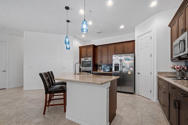 kitchen with light stone countertops, pendant lighting, stainless steel appliances, an island with sink, and a breakfast bar