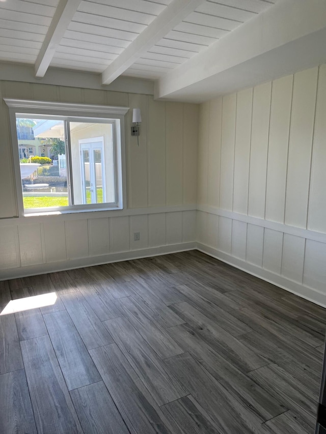 spare room featuring dark wood-style floors, a decorative wall, and beam ceiling