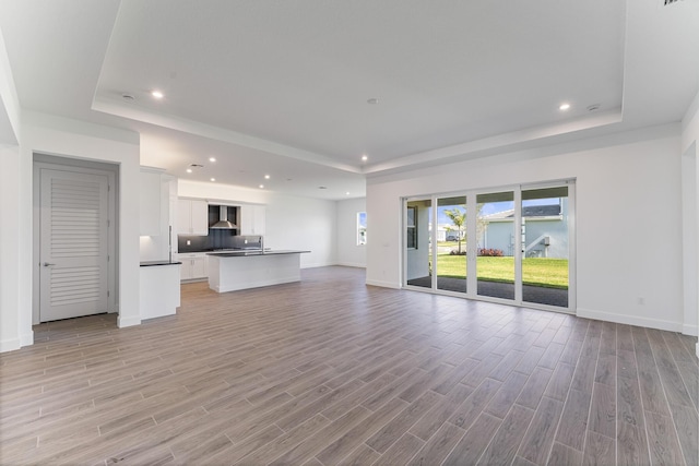 unfurnished living room featuring a tray ceiling and light hardwood / wood-style floors