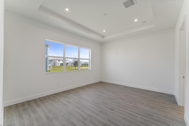 spare room featuring a tray ceiling and light wood-type flooring