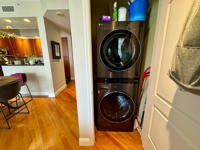 clothes washing area featuring stacked washer and dryer and light hardwood / wood-style flooring