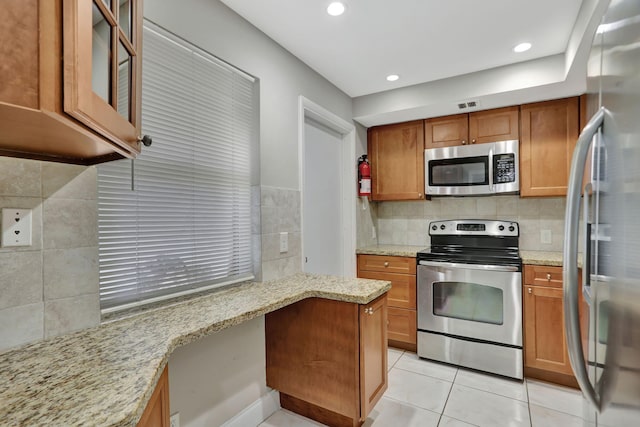 kitchen featuring light stone countertops, stainless steel appliances, tasteful backsplash, kitchen peninsula, and light tile patterned floors