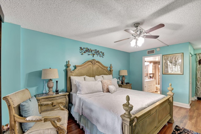 bedroom with a textured ceiling, wood-type flooring, ceiling fan, and ensuite bath