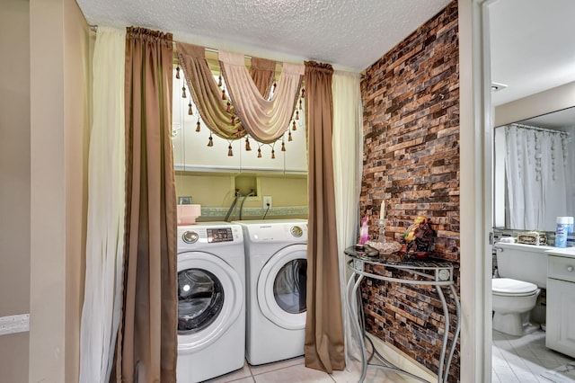 laundry area featuring light tile floors, hookup for a washing machine, washing machine and dryer, a textured ceiling, and brick wall