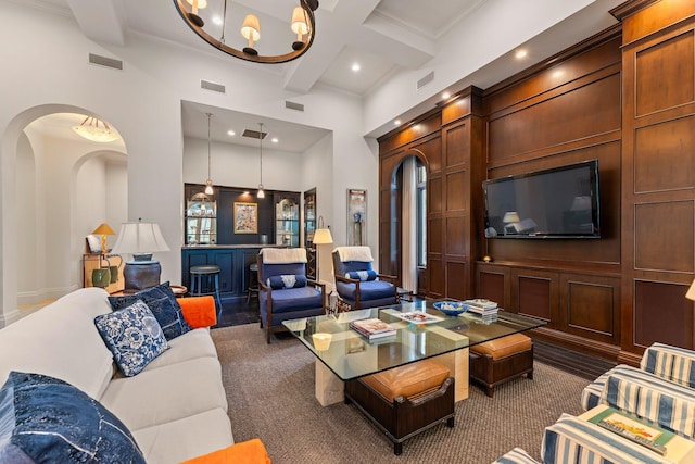 living room featuring a notable chandelier, a towering ceiling, ornamental molding, and beam ceiling