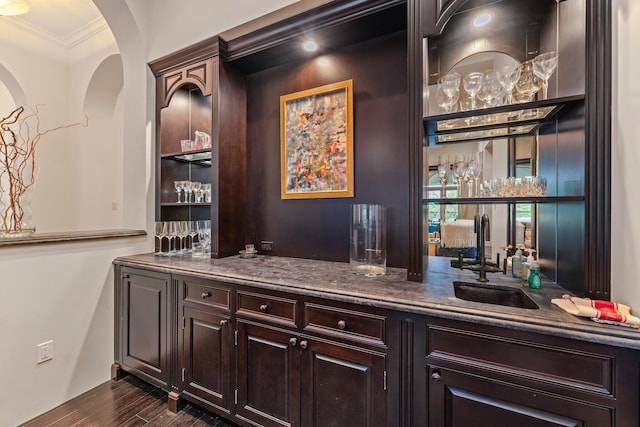 bar with dark brown cabinetry, dark hardwood / wood-style floors, stone counters, ornamental molding, and sink