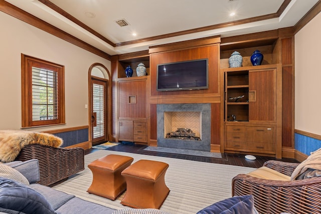 living room featuring dark hardwood / wood-style floors, crown molding, a premium fireplace, a raised ceiling, and built in shelves