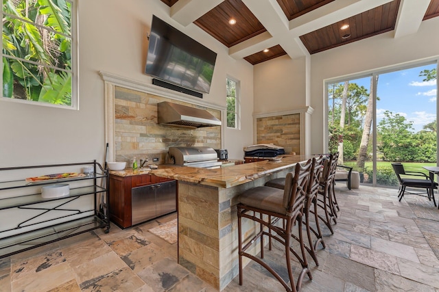 kitchen featuring light tile floors, wall chimney exhaust hood, wood ceiling, and coffered ceiling