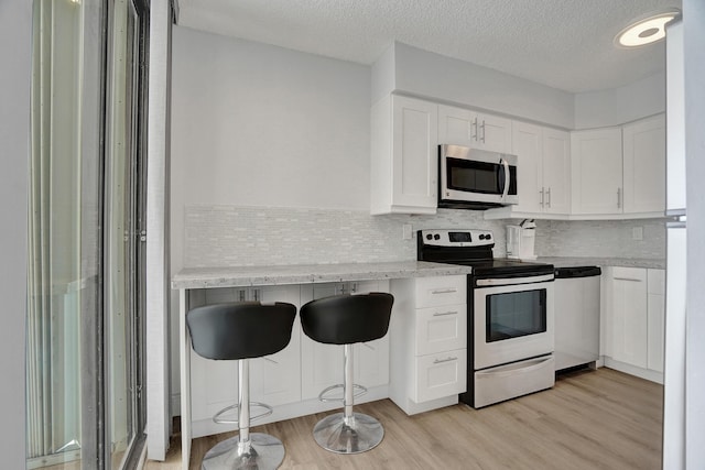 kitchen featuring a kitchen breakfast bar, light wood-type flooring, white cabinetry, and stainless steel appliances