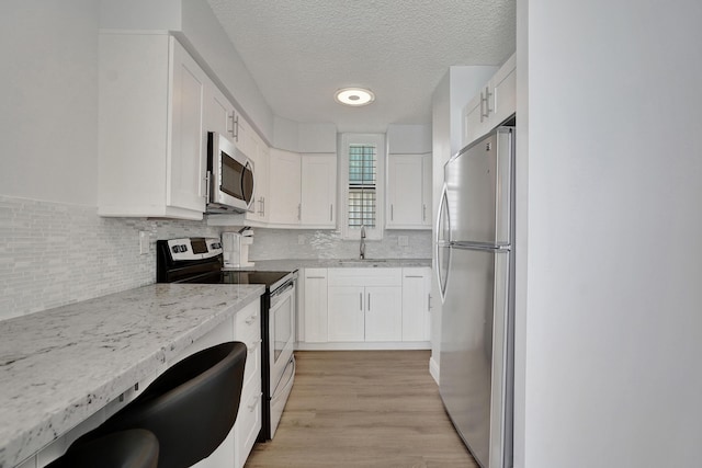 kitchen featuring sink, light wood-type flooring, a textured ceiling, appliances with stainless steel finishes, and white cabinetry