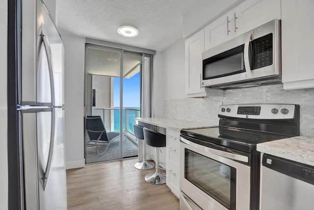 kitchen featuring white cabinets, light stone counters, a water view, and appliances with stainless steel finishes