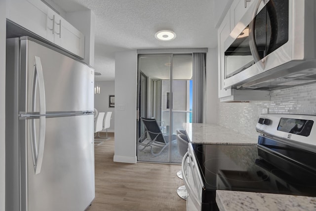 kitchen with white cabinets, light stone countertops, stainless steel appliances, and light hardwood / wood-style flooring