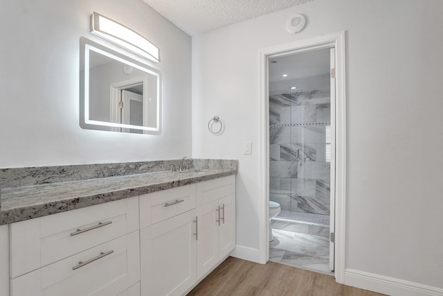 bathroom featuring vanity, hardwood / wood-style flooring, toilet, a textured ceiling, and a shower with shower door