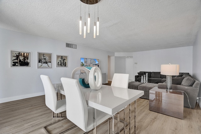 dining area featuring a textured ceiling, light hardwood / wood-style flooring, and a chandelier