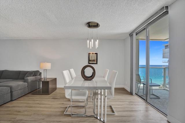 dining area with expansive windows, a water view, light wood-type flooring, and a textured ceiling