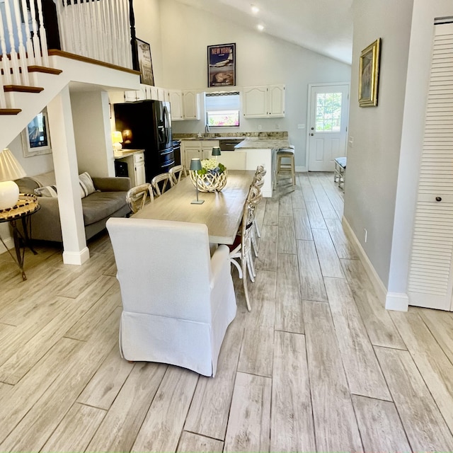 dining room with high vaulted ceiling, sink, and light wood-type flooring